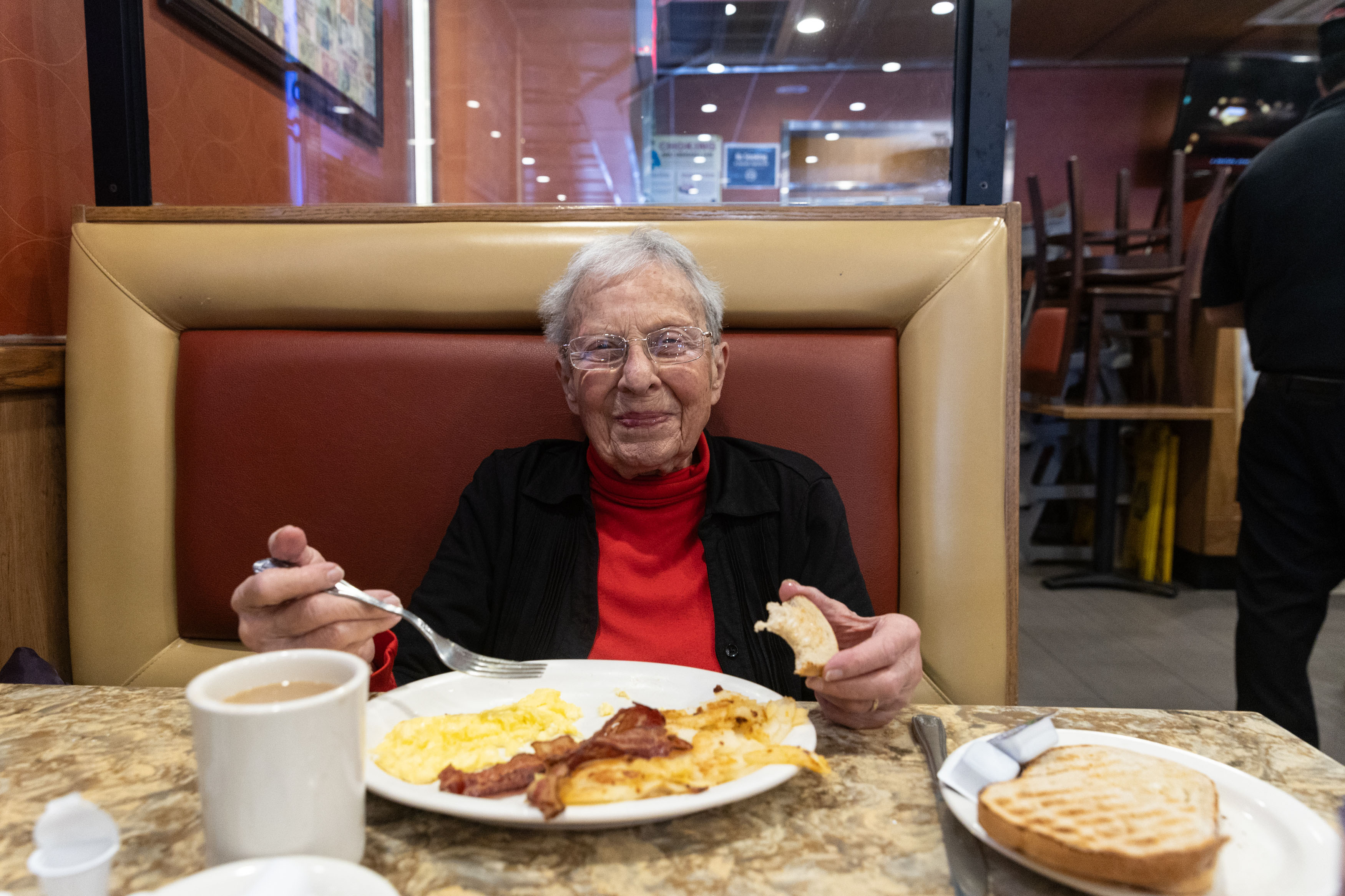 A portrait of a senior woman smiling as she eats breakfast at a New York City diner.